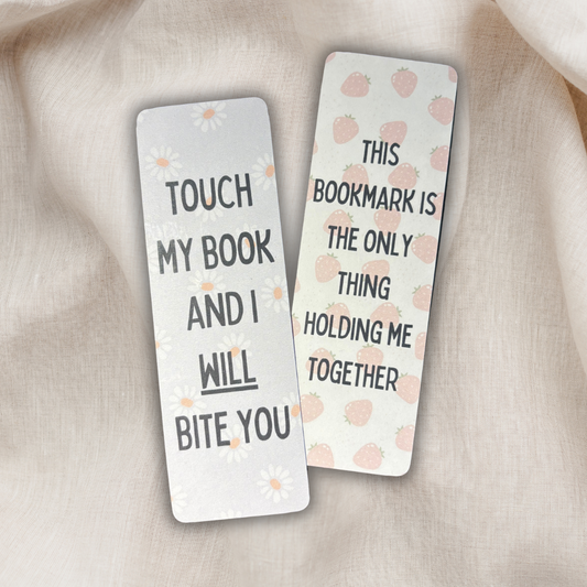 Double-sided laminated cardstock bookmark with sassy quotes – ‘Touch my book and I will bite you’ on one side with daisy background, and ‘This bookmark is the only thing holding me together’ on the other side with pink strawberry design. Funny handmade bookish gift and reading accessory.