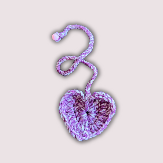 Crocheted heart-shaped keychain with a pink and purple pattern on a light pink background